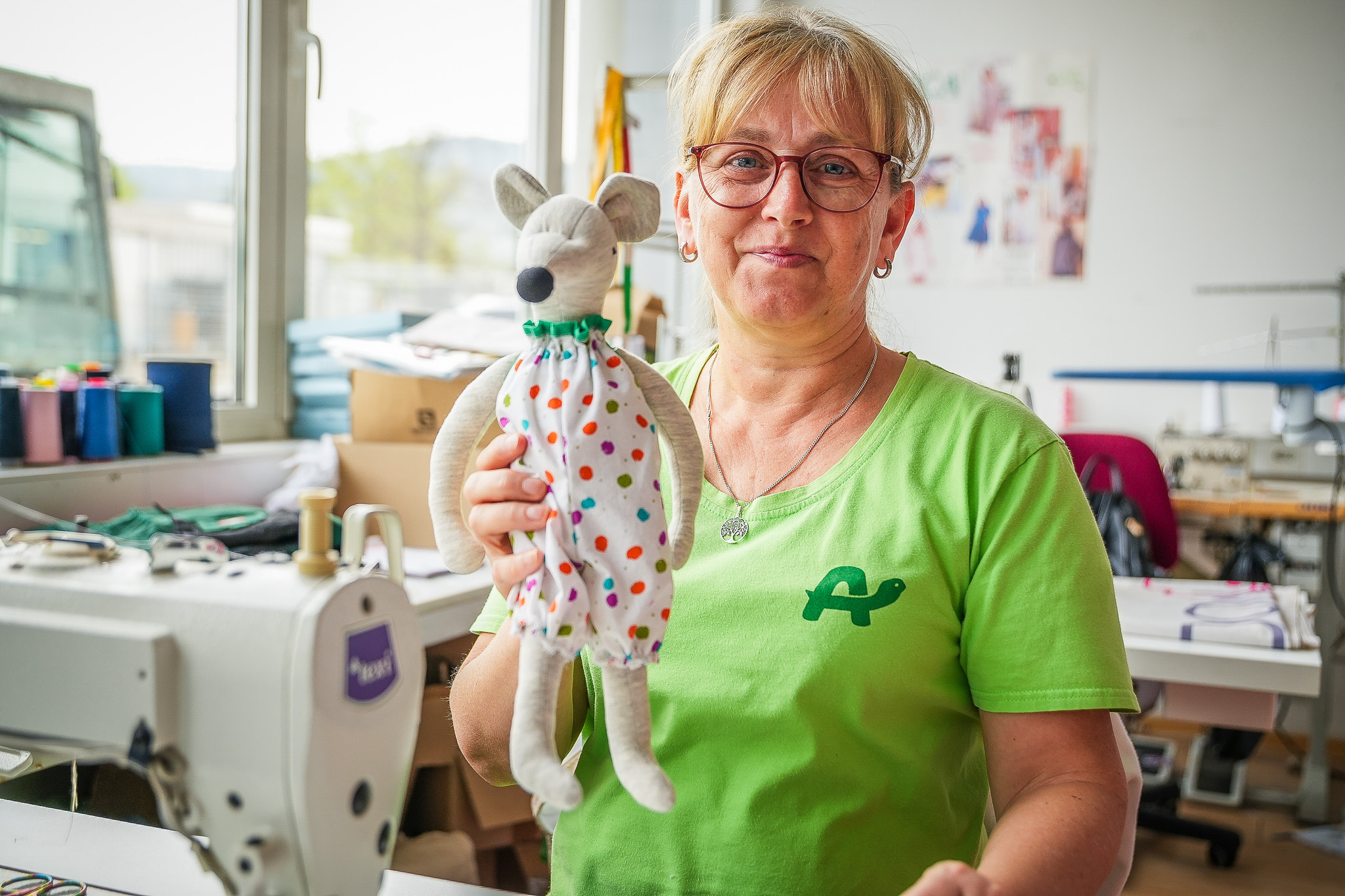 Delavka za šivalnim strojem v roki drži igračko iz blaga in predstavlja Želvin krog vključevanja.