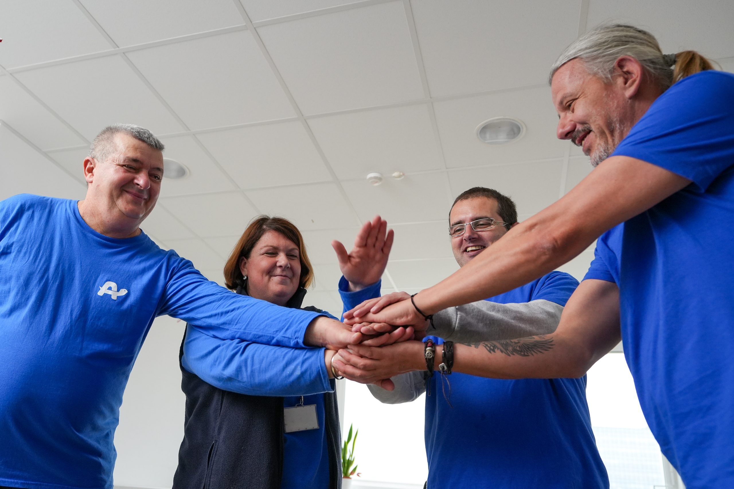 Ekipa nasmejanih sodelavcev v službenih oblačilih modre barve s polaganjem rok na en kup prikazuje sodelovanje in ekipni duh.