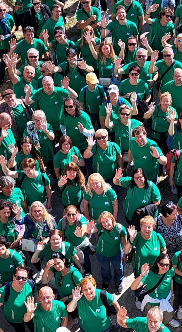 Velika skupina zaposlenih v enakih majicah zelene barve, ki nasmejani mahajo v objektiv kamere.